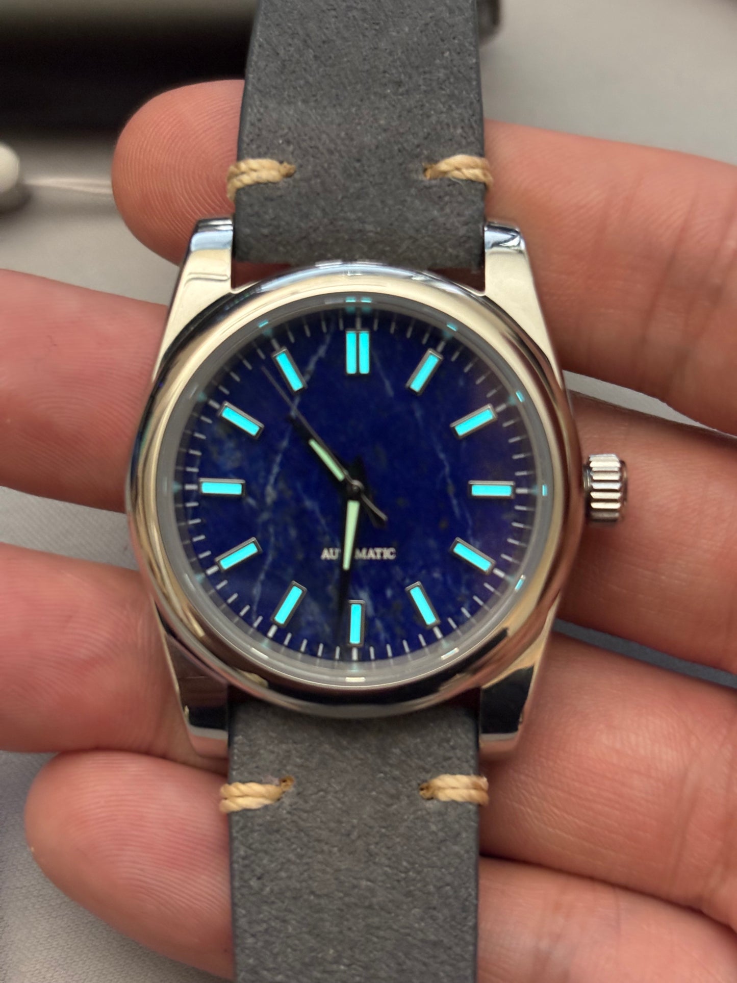 Watch with blue face and gray strap held in hand Lapis Lazuli