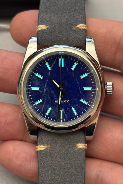 Wristwatch with blue dial and gray strap held in hand