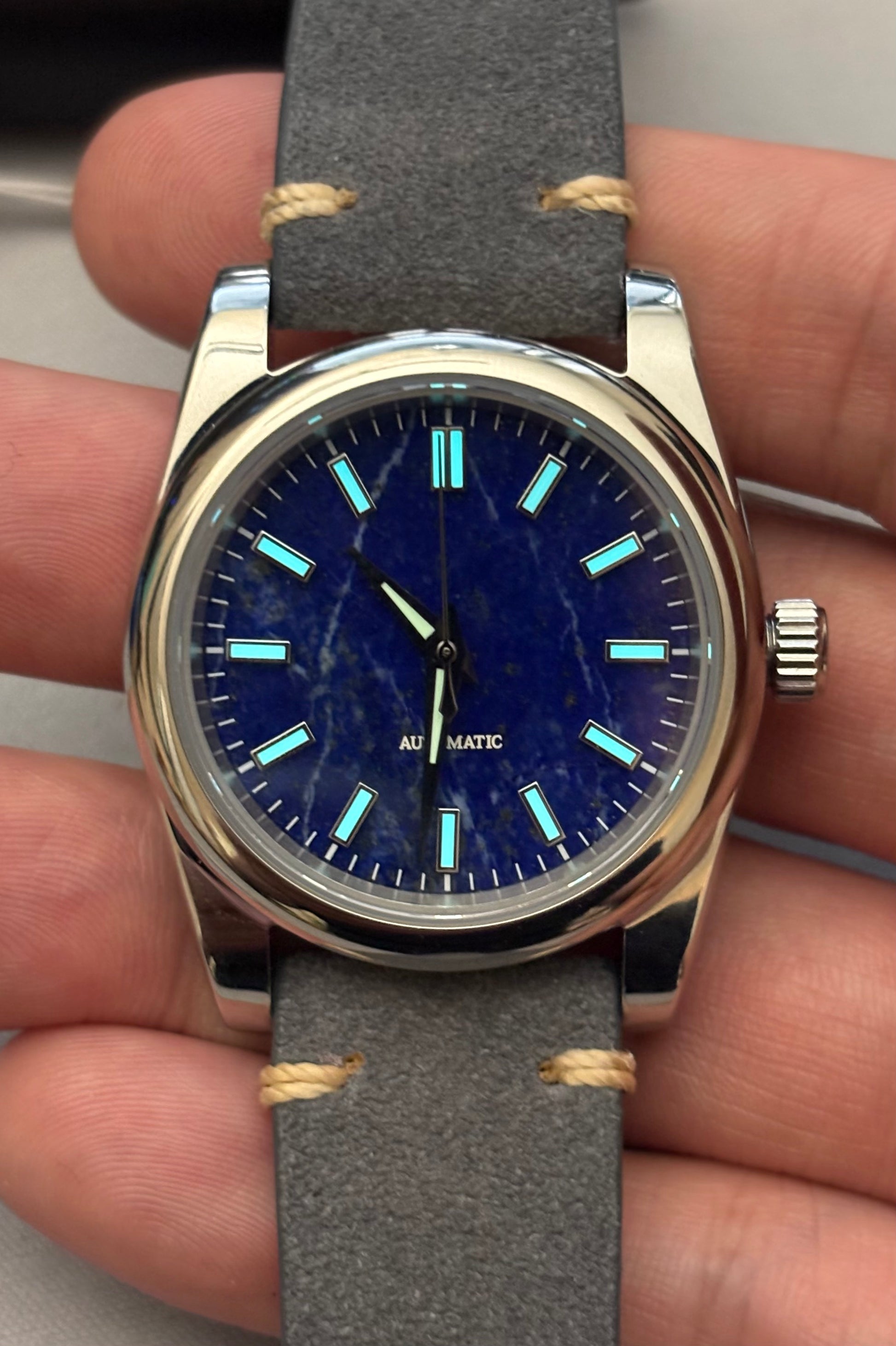 Wristwatch with blue dial and gray strap held in hand Lapis Lazuli