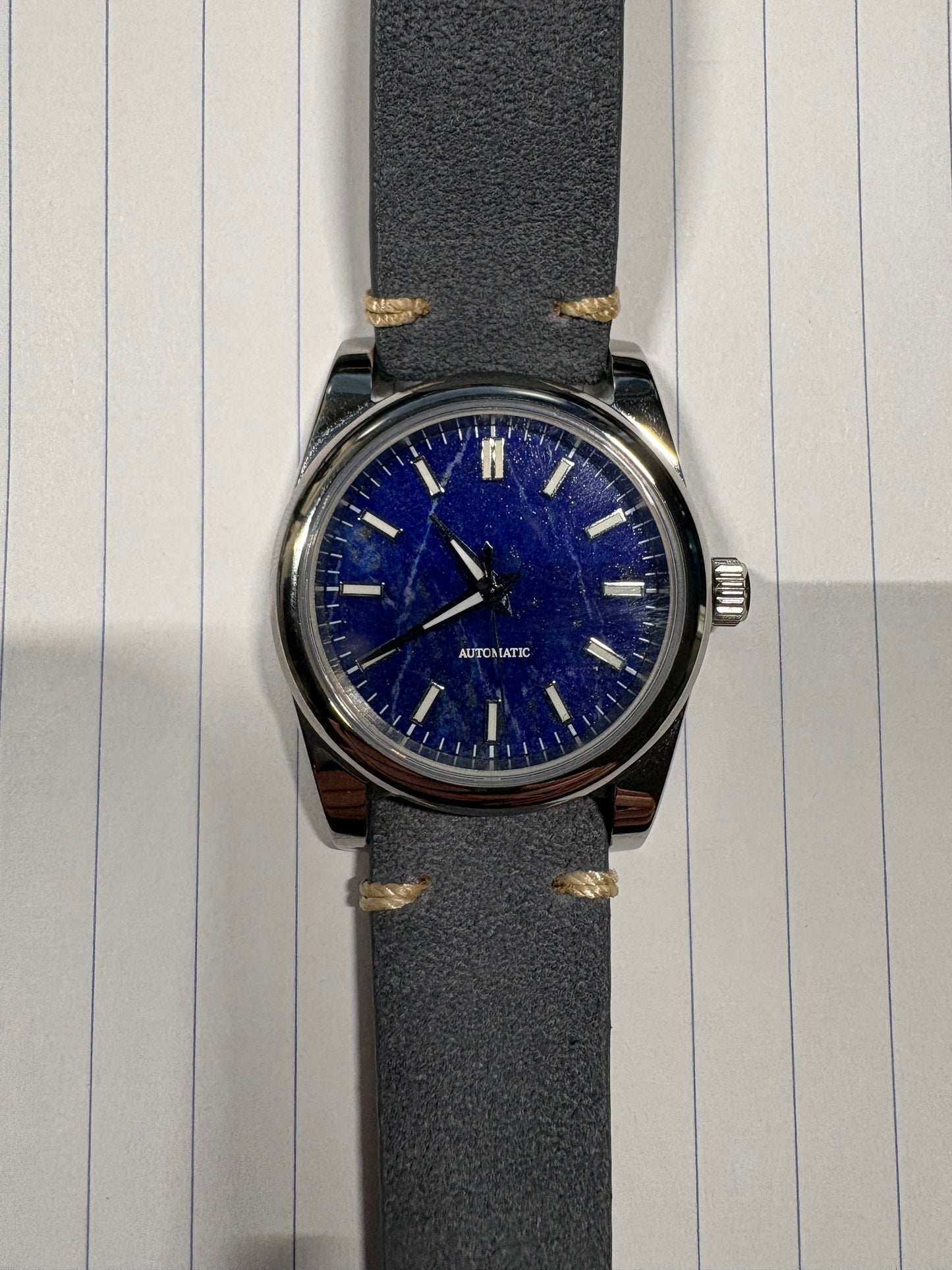 Watch with a blue face and gray strap on lined paper Lapis Lazuli dial