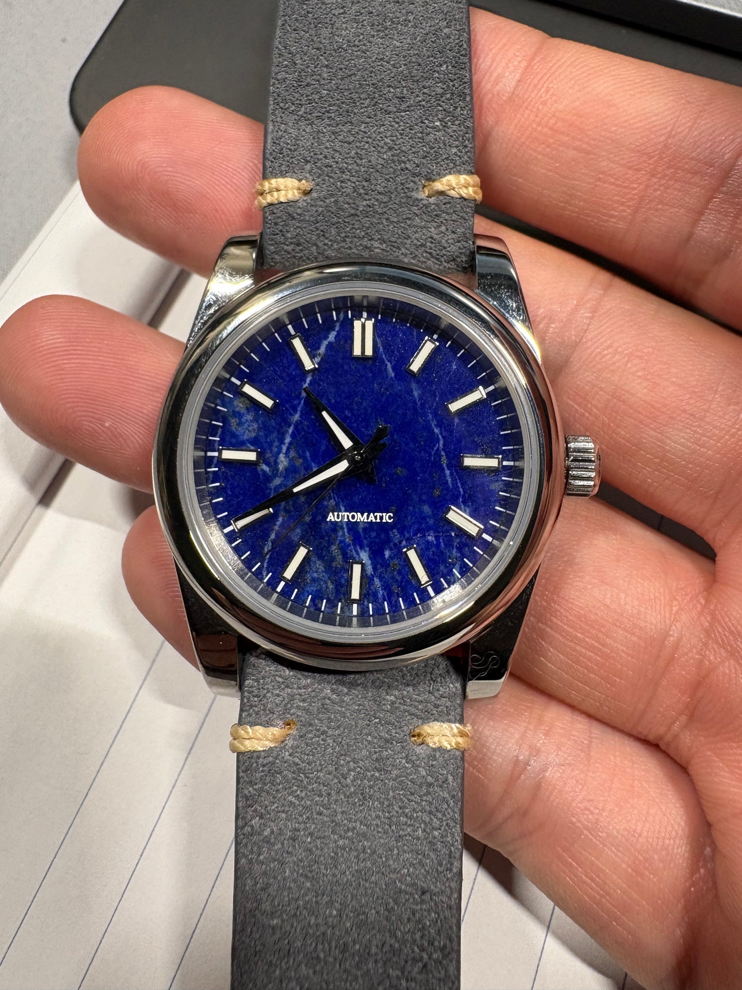 Hand holding a watch with a blue stone Lapis Lazuli dial and gray strap 